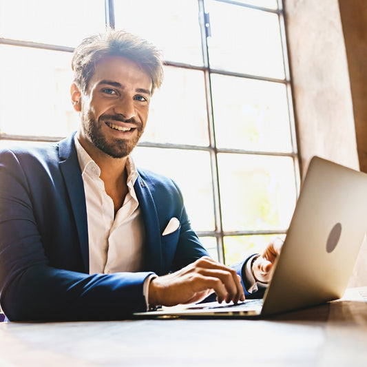 Man types on his laptop, smiles at the camera.